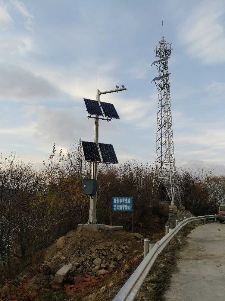 Solar-powered fire surveillance camera pole on forest road with backup battery station