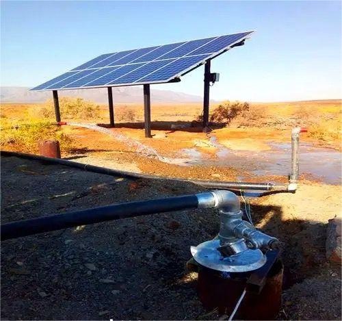 A solar-powered pump extracts water from a remote well in desert farmland, supporting crops where grid power is unavailable