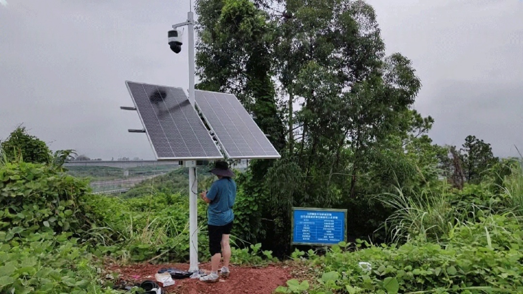 A solar-powered CCTV system with dual panels installed near a riverbank ensures continuous environmental and security monitoring in remote areas of China
