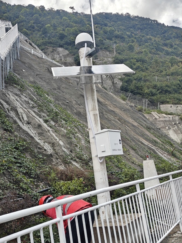 On-site installation of an off-grid solar power system supporting GNSS slope monitoring on a steep hydropower slope in Weixi, Yunnan, illustrating compact mounting, protected enclosure placement, and safe maintenance under high-humidity conditions